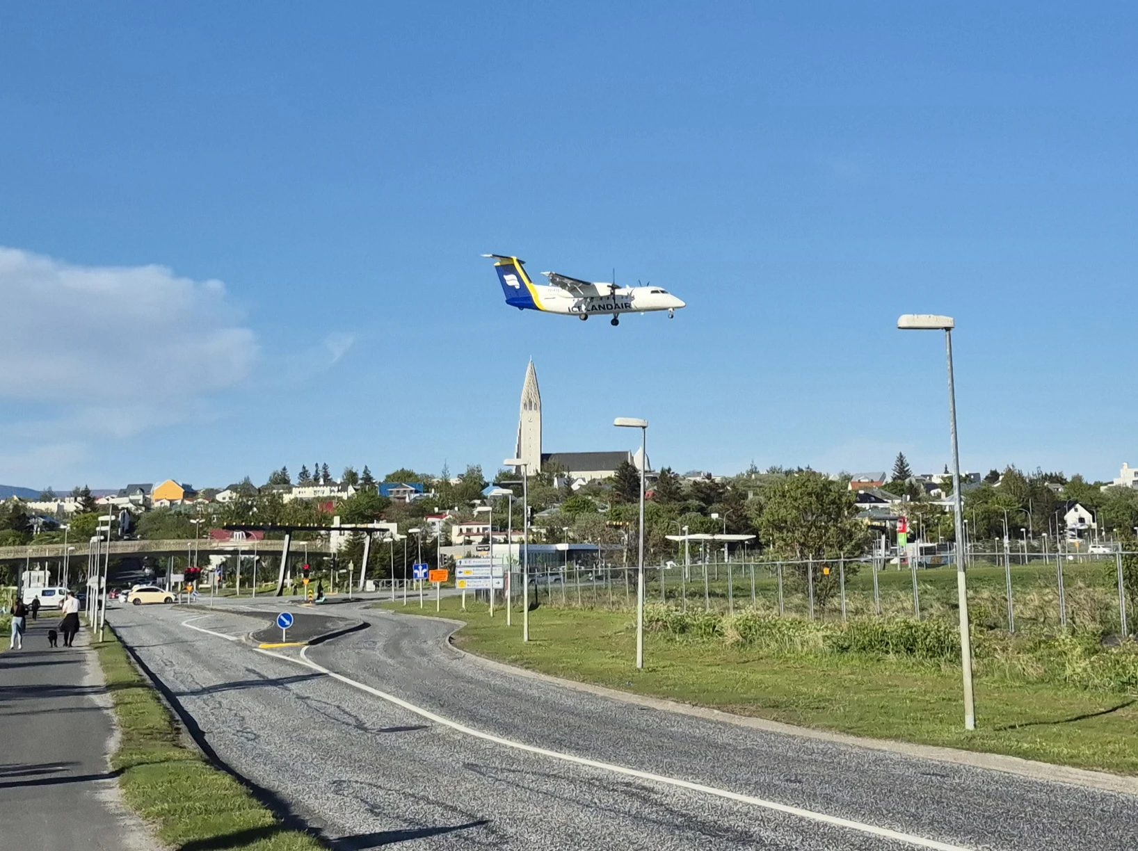 An airplane descending toward a runway with trees and buildings in the background, likely at Reykjavík Domestic Airport