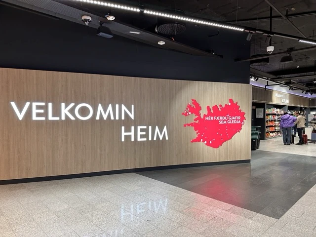 A welcome sign at Keflavík Airport with the text “VELKOMIN HEIM” (Welcome Home) and a pink map of Iceland.