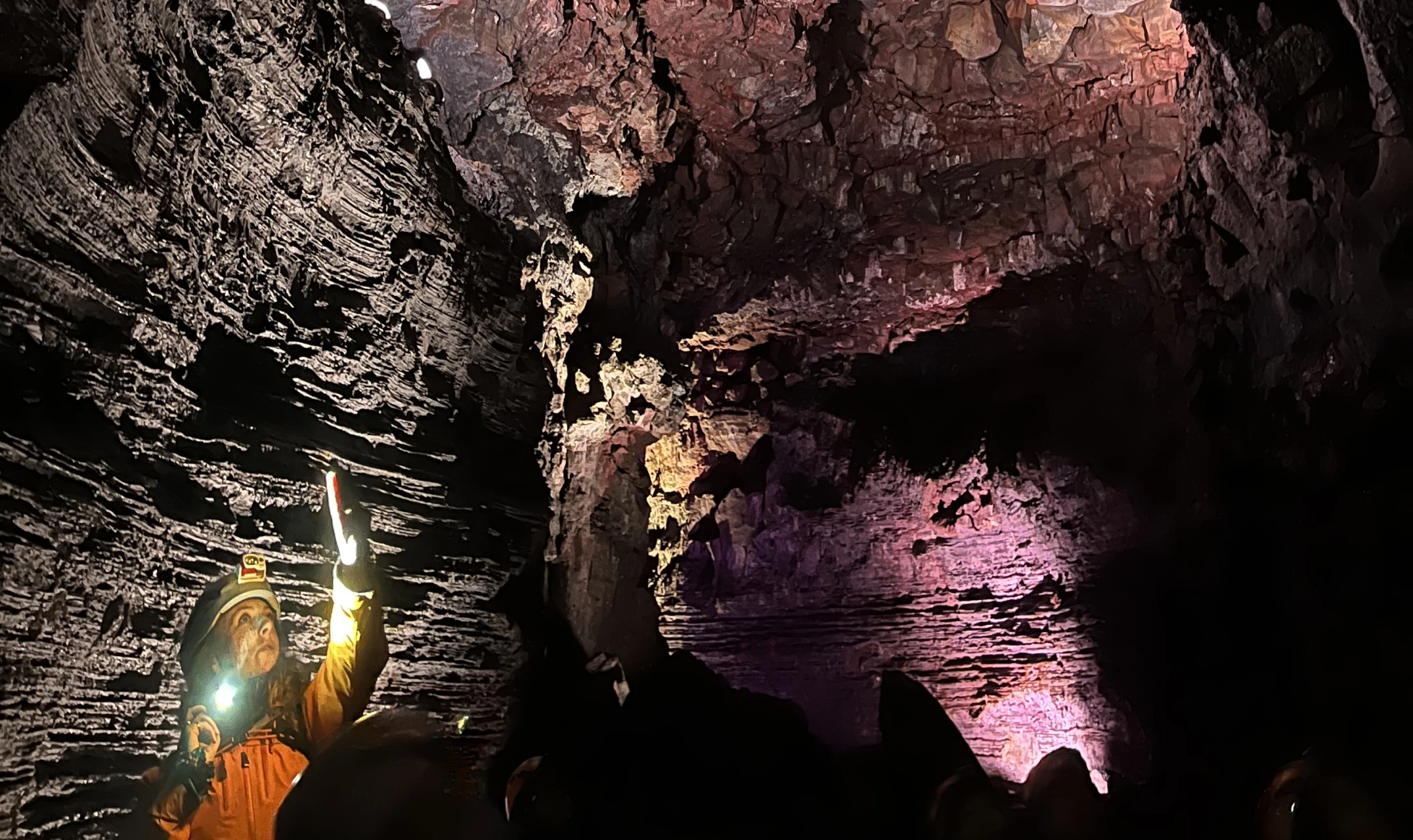 A group explores a lit-up lava cave or magma tunnel with pink and yellow lighting, evoking adventure and team bonding.