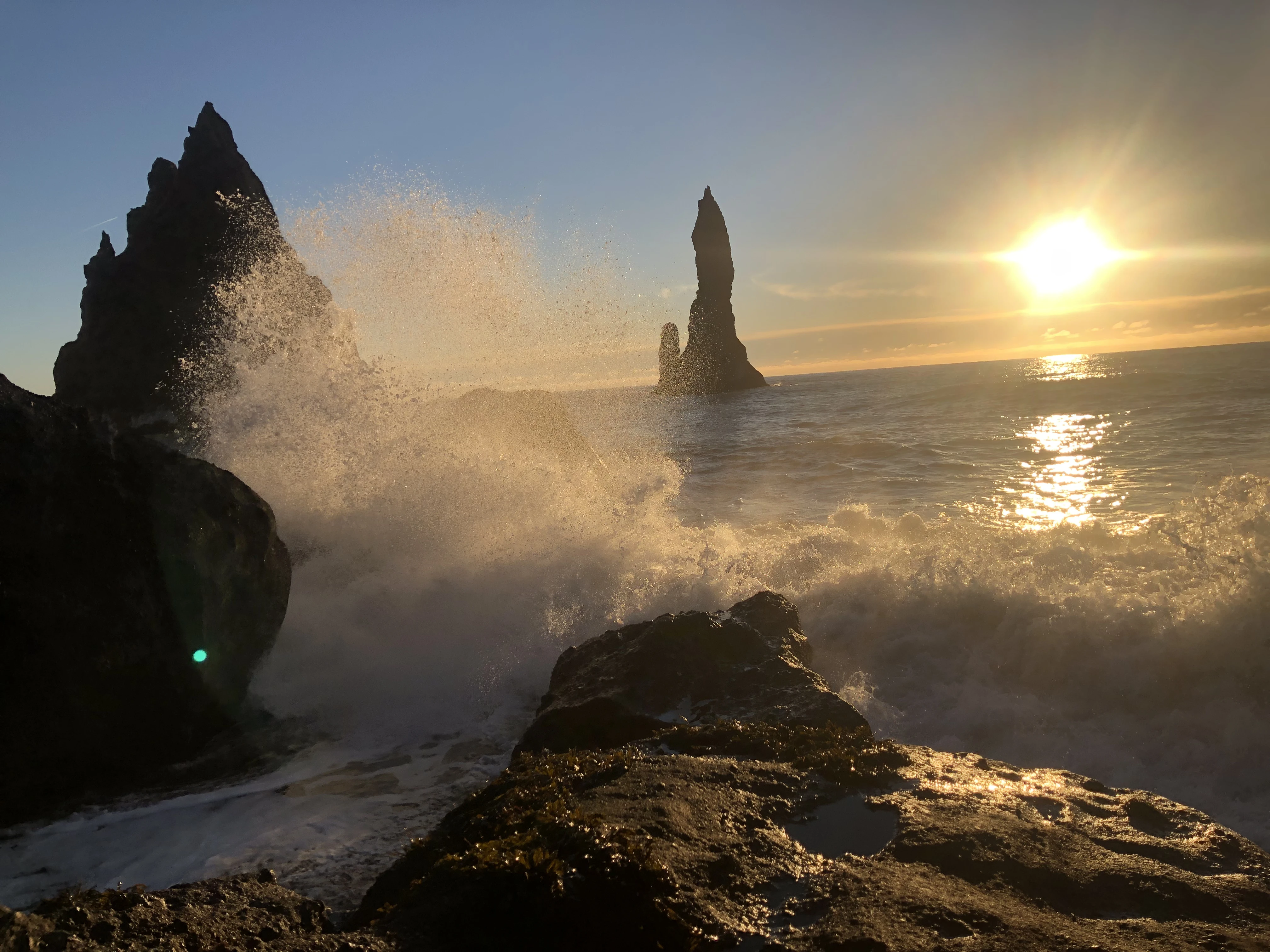Dramatic ocean waves crash against black rock spires at Reynisfjara beach under golden light, evoking a romantic and powerful atmosphere.