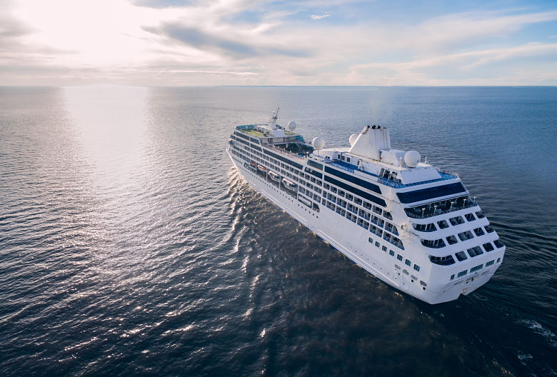 A white cruise ship sailing across a calm ocean at sunset.